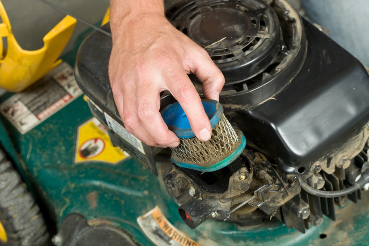 A person is removing a dirty air filter from the inside of a lawn mower.