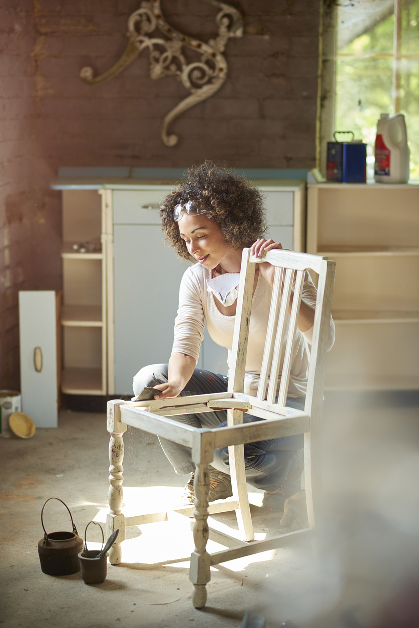 woman in workshop wiping an antique white wooden chair frame with a tack cloth