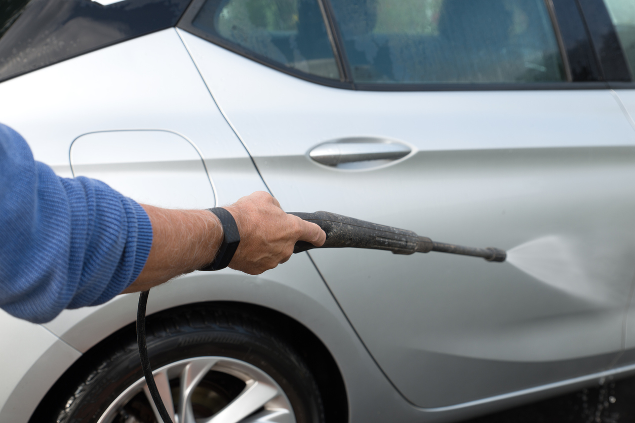 close up of man using a pressure washer to wash a gray car