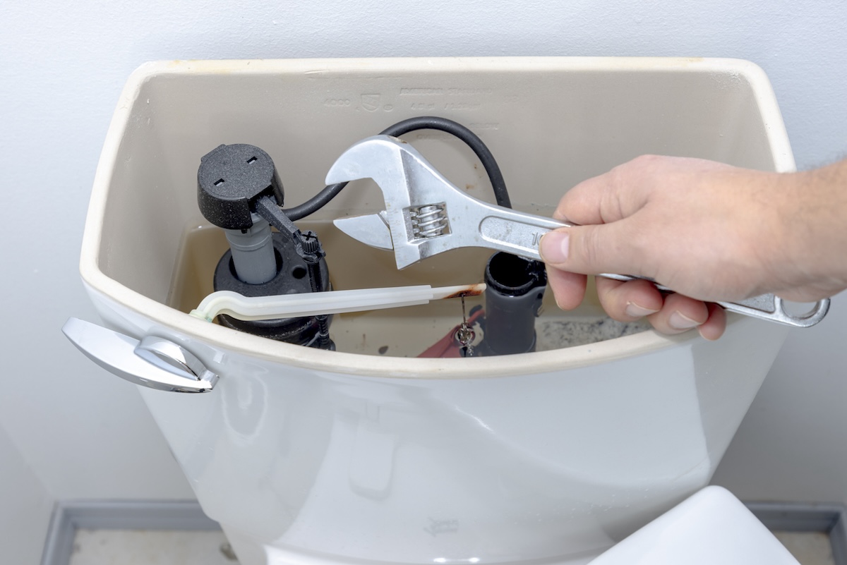 A person holding a wrench near an open toilet tank to make a diy plumbing repair.