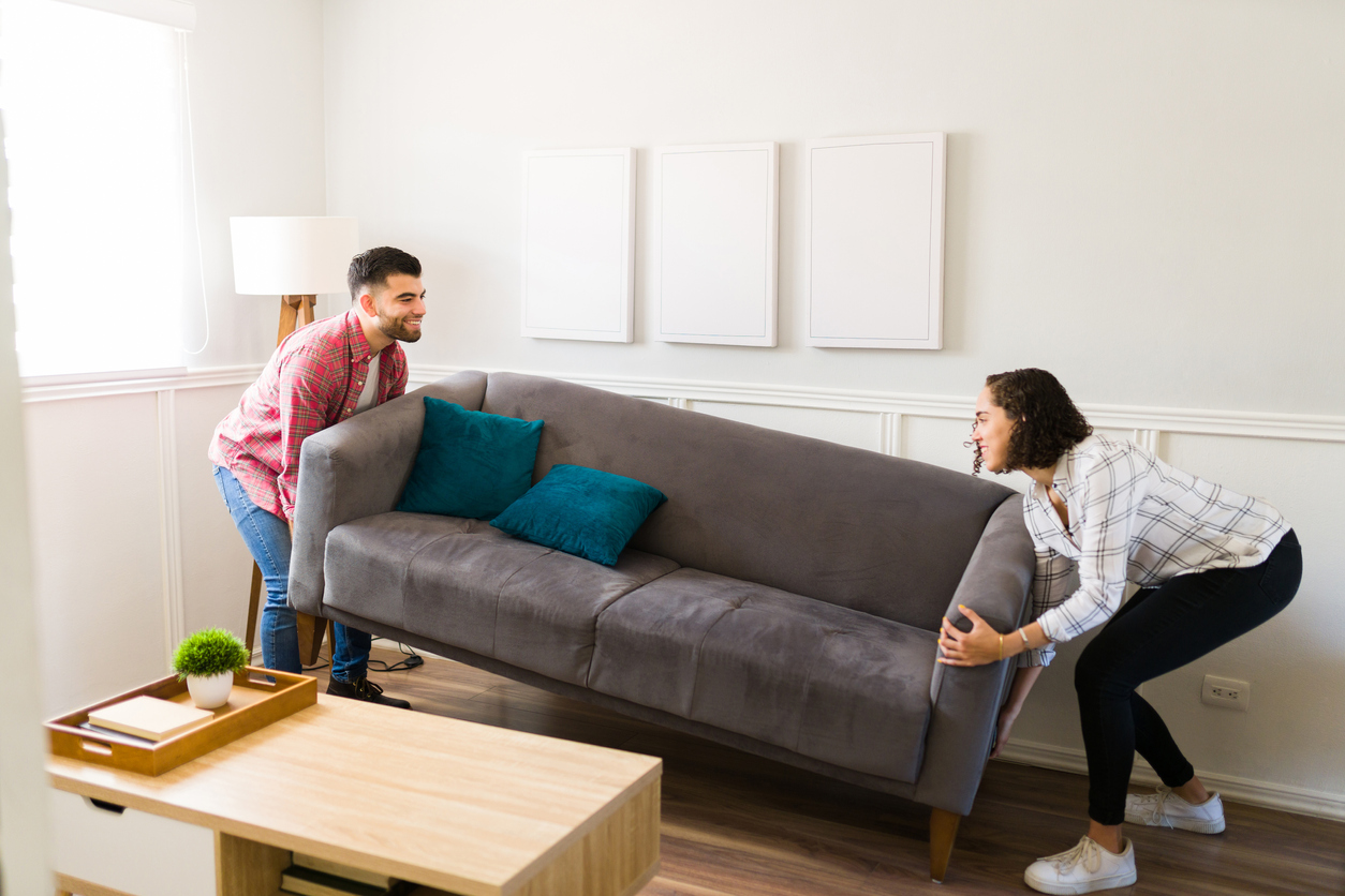 Cheerful young couple doing home improvements and moving their sofa in the living room while decorating