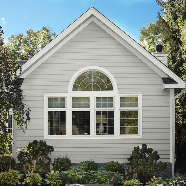 An exterior wall of a house with a window is painted pale grey.