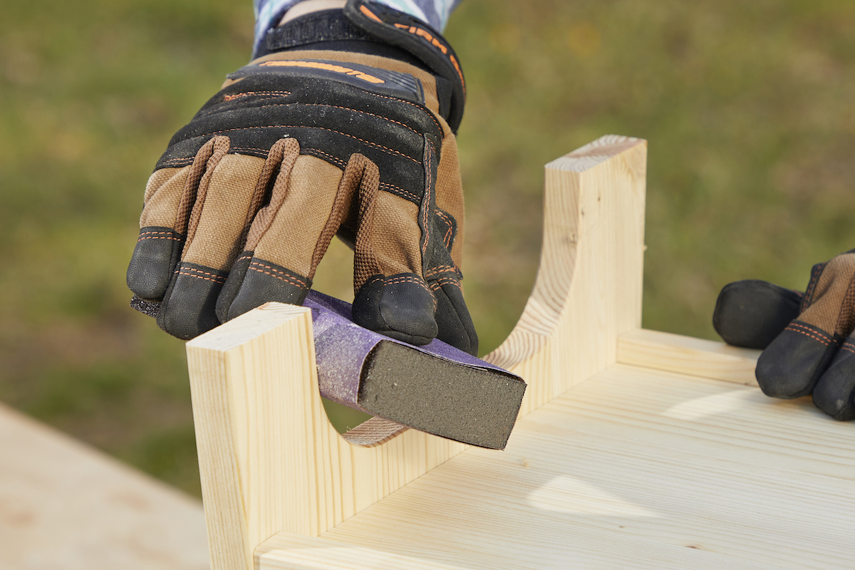 Woman sands a curved piece of wood with a sanding block.