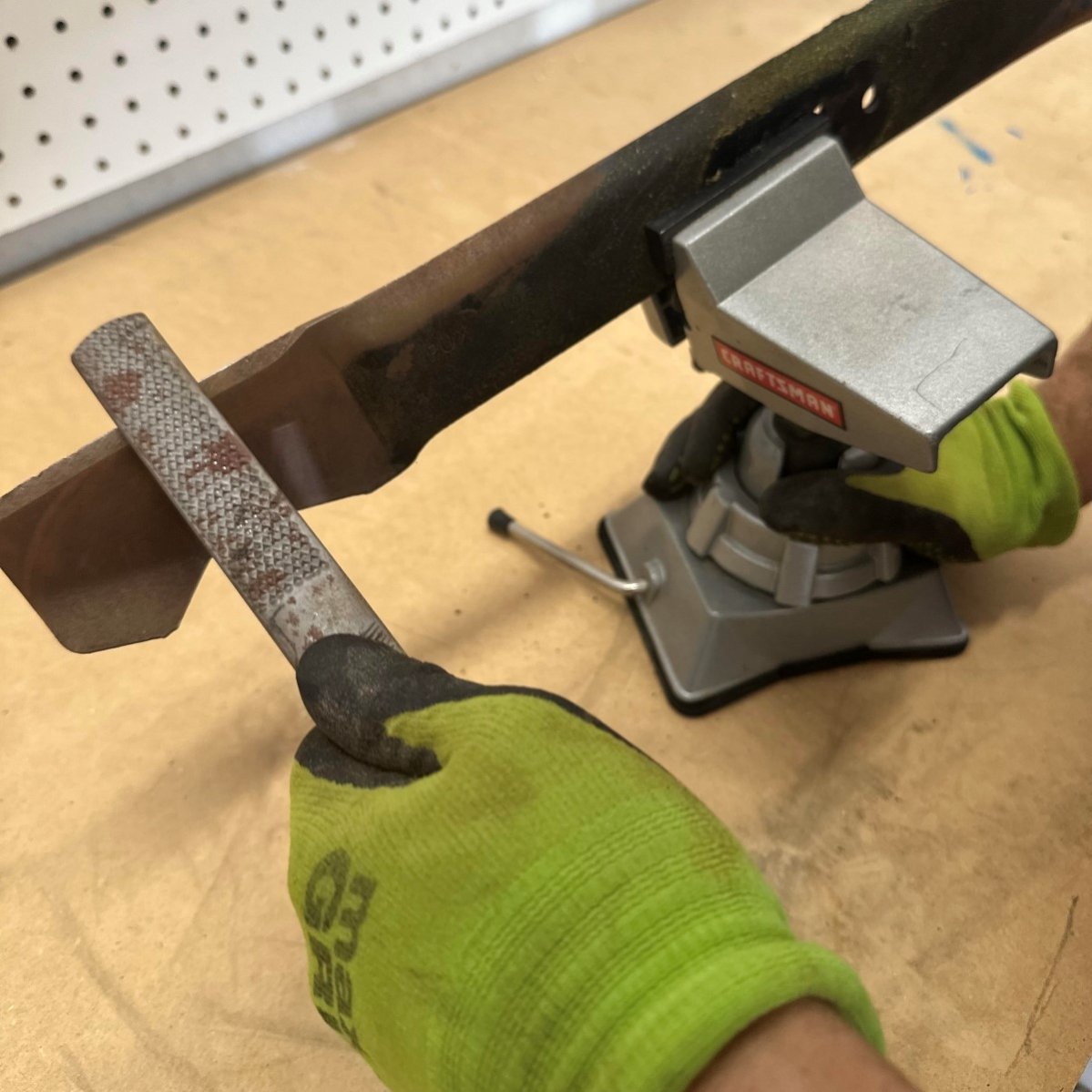 Person using a tool to sharpen lawn mower blade.