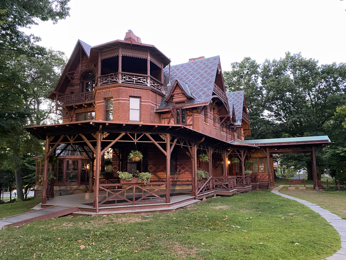 une maison gothique victorienne en briques rouges avec un porche enveloppant et entourée d'arbres