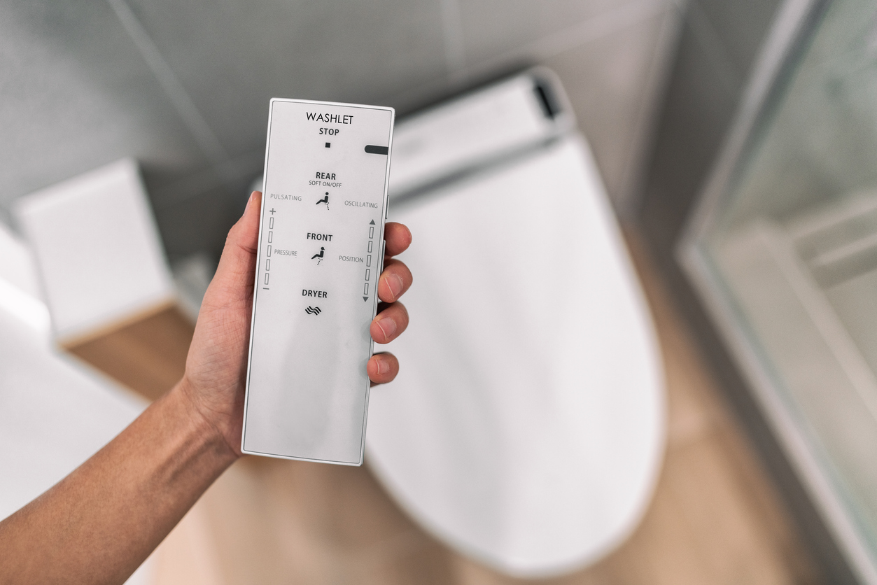 Une main tient un contrôle à distance pour le bidet au-dessus de la toilette dans une salle de bain moderne.