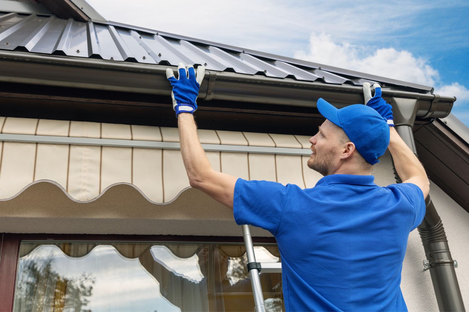 Un homme vêtu de bleu installe un protège-gouttière.