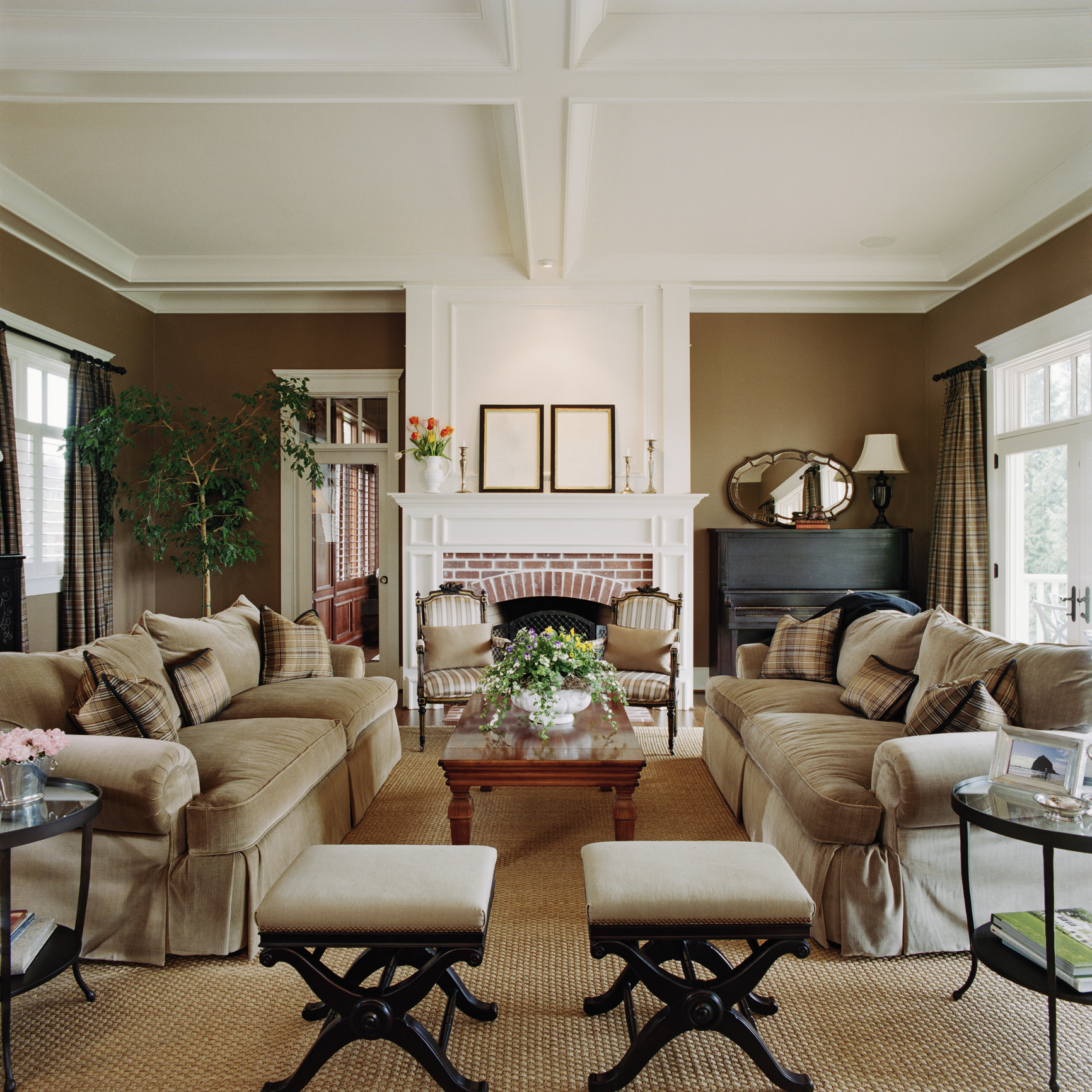 A regal living room with a tray ceiling is furnished with matching beige couches, chairs, and stools.