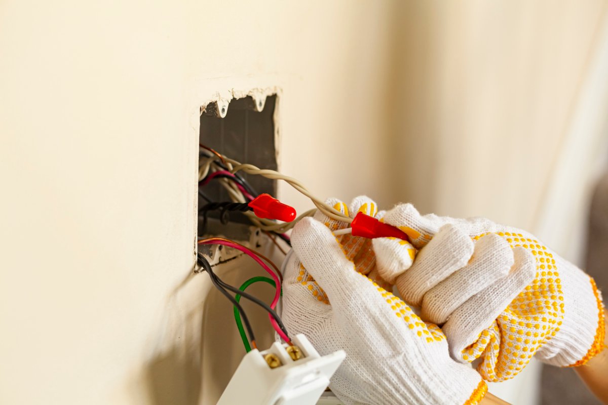 Electrical system in a wall being repaired by person in gloves.