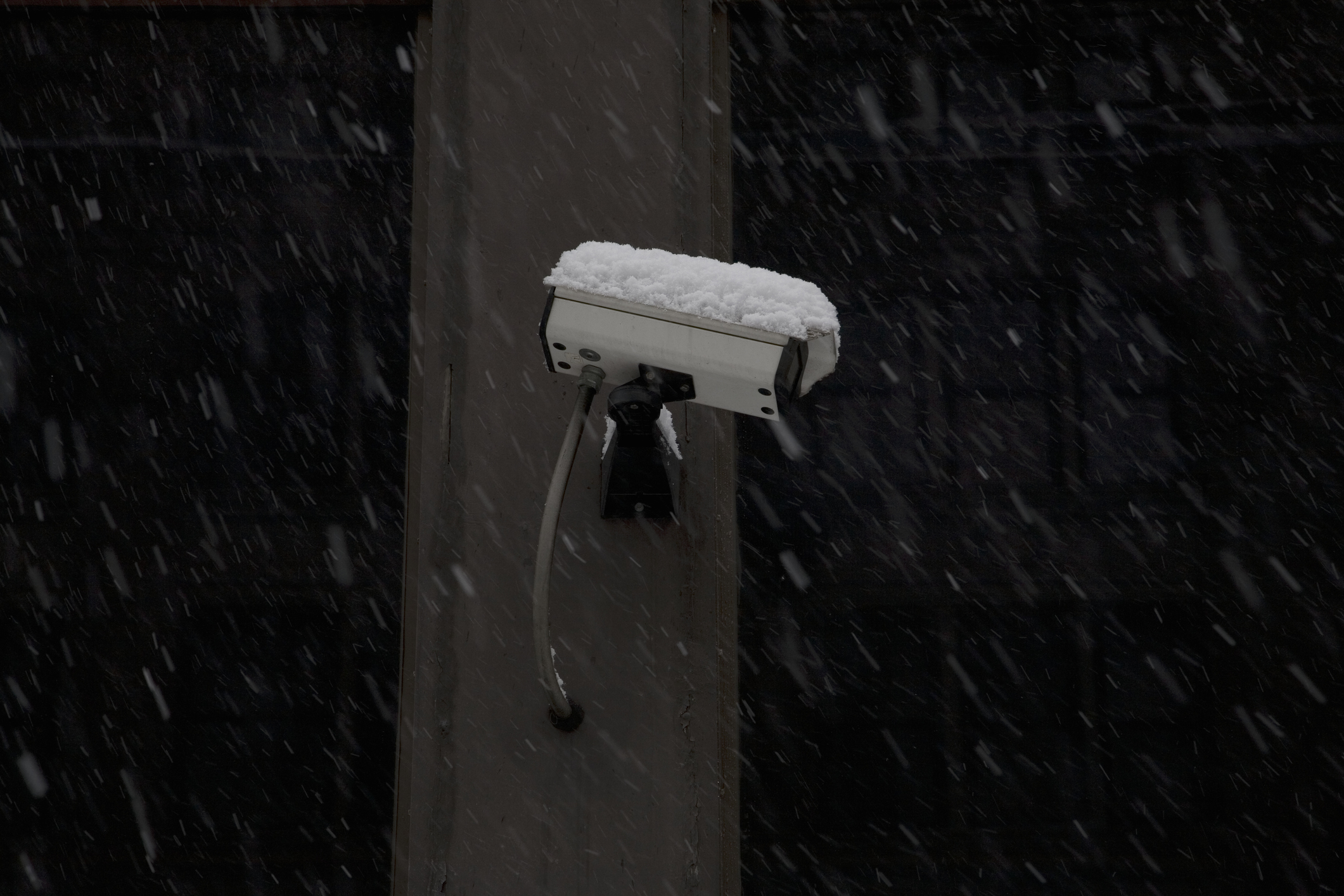 Outdoor security camera covered with snow with snow falling in the background.