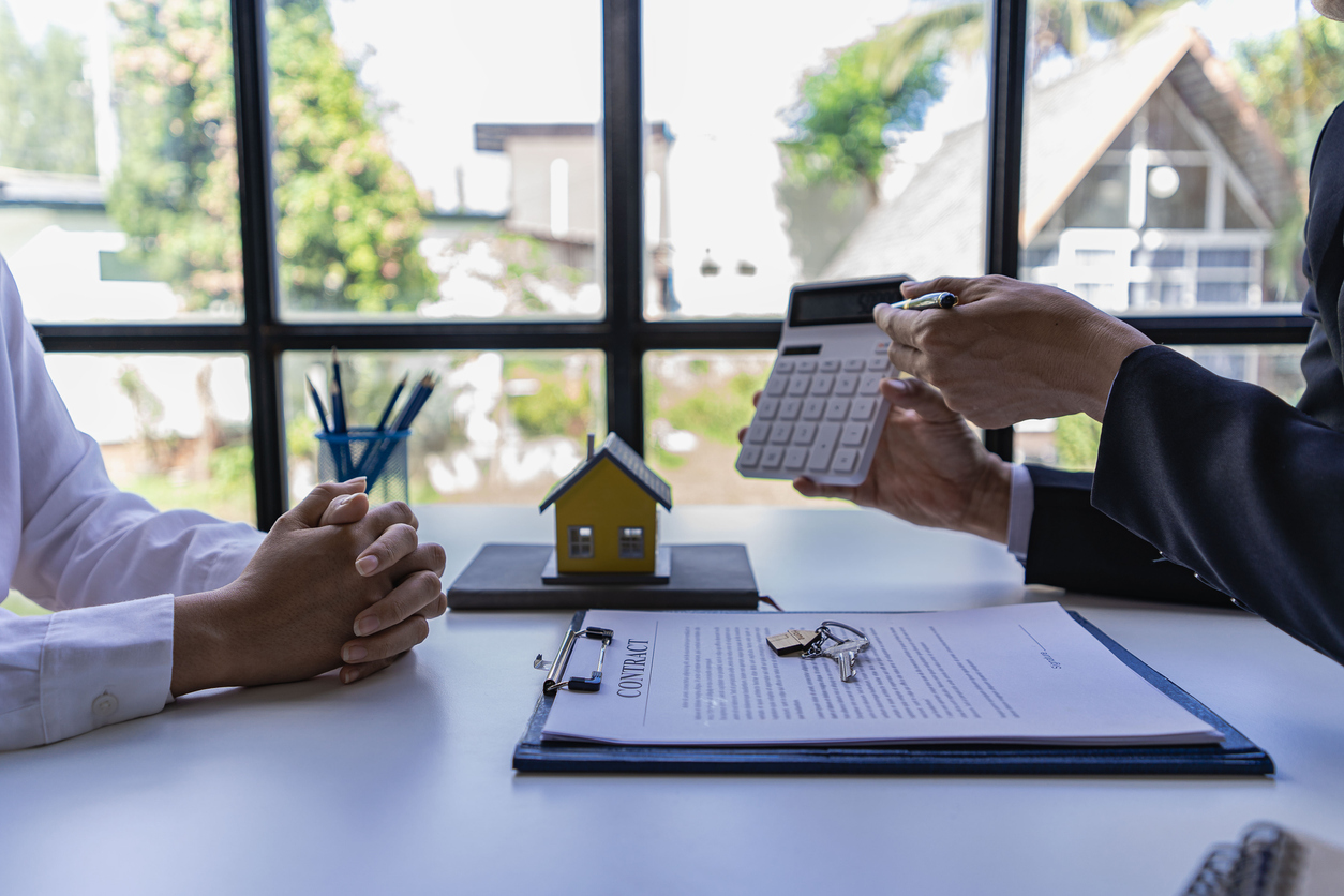 un homme tenant une calculatrice pour montrer à quelqu'un d'autre une maison sur la table illustrant un concept immobilier