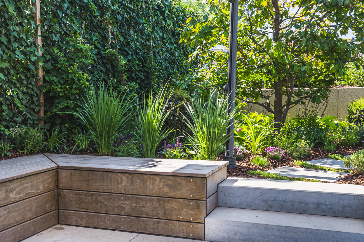 Concrete garden bench in yard with leafy landscaping.