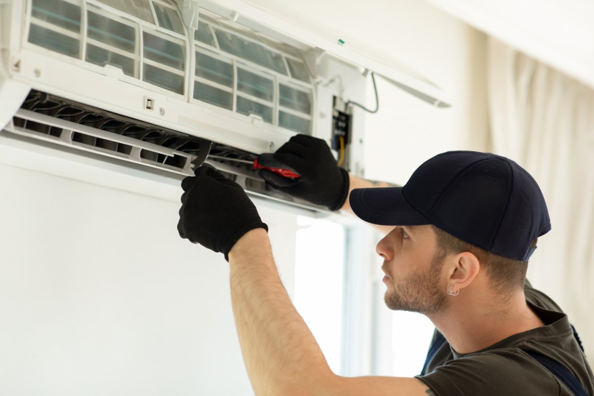 A repairman fixes a wall-mounted AC unit wit a hand tool. 