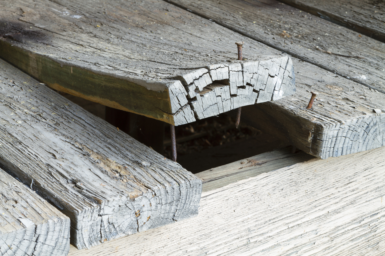 A set of old, cracked, peeling exterior deck board planks on a home with one that has warped alot and is curling up from exposure to the elements outside.