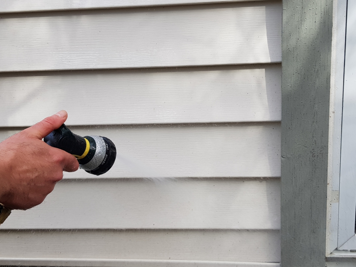 Using hose to wash vinyl siding.