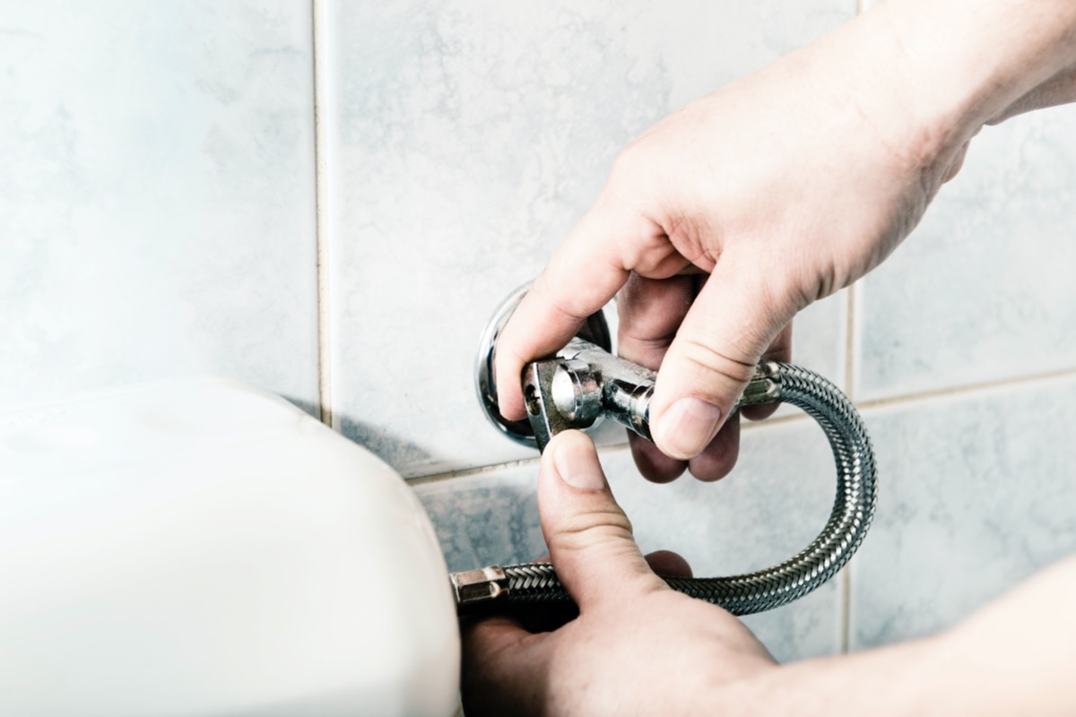 Person turning off toilet's water valve. 