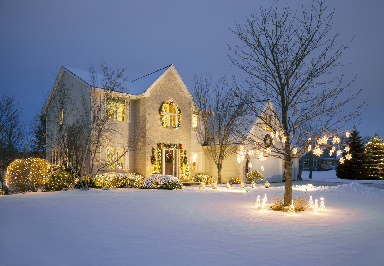 Une maison en briques blanches décorée de lumières de Noël blanches et d'une grande pelouse recouverte de neige.