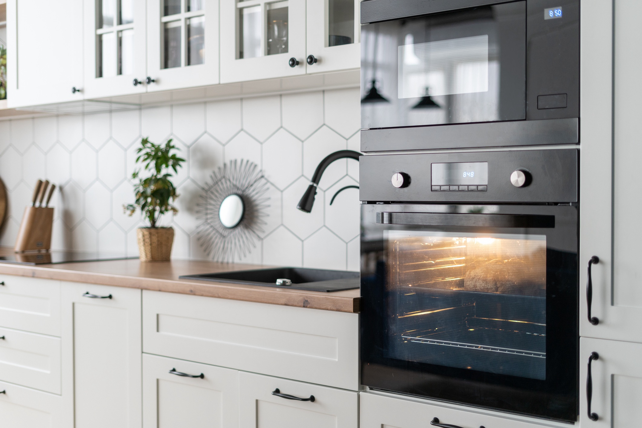 Side view of contemporary black oven kitchen interior design. Stylish white wood furniture surface with appliances and decor. Cozy place for cooking. Baking process