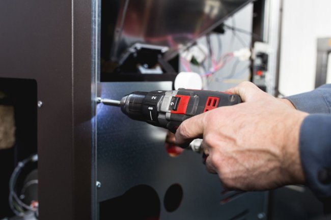 A close up of hands using a tool to install a pellet stove. 