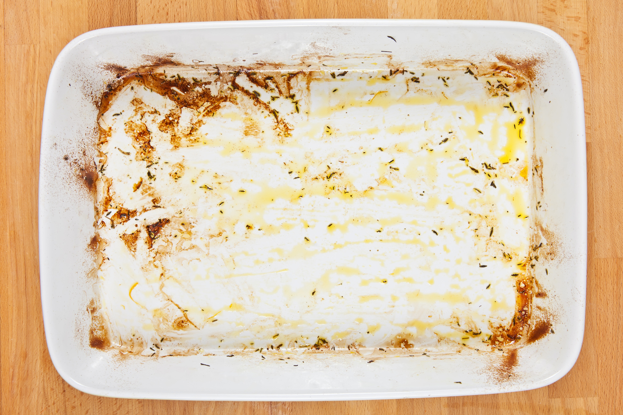 Greased ceramic tray with remains of olive oil and burnt food after roasting food in the oven.