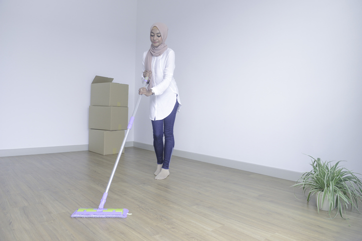 empty-room-with-woman-in-beige-hijab-and-white-shirt-with-jeans-cleaning-floor-with-swiffer-and-boxes-nearby