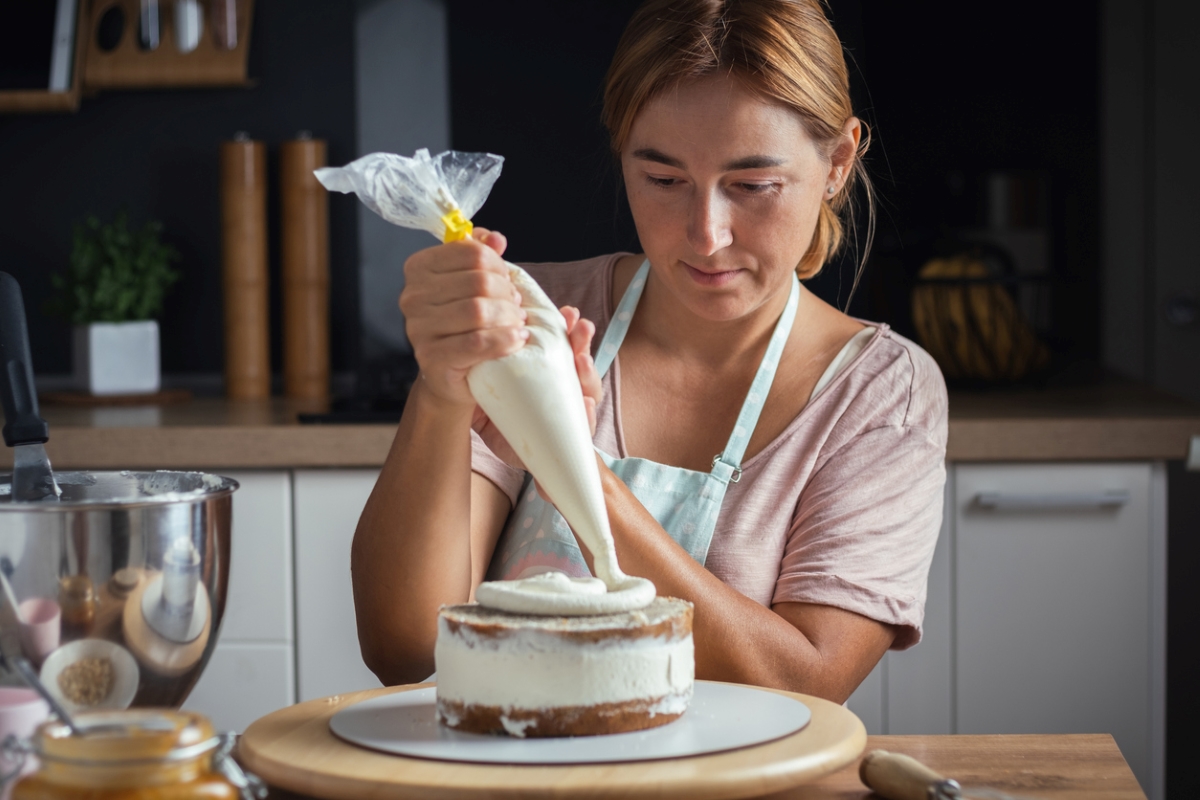 Woman using plastic bag to frost cake.