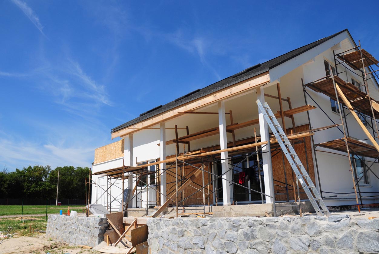 A home addition is being built onto the back of a home, while the side of the home is covered by scaffolding.