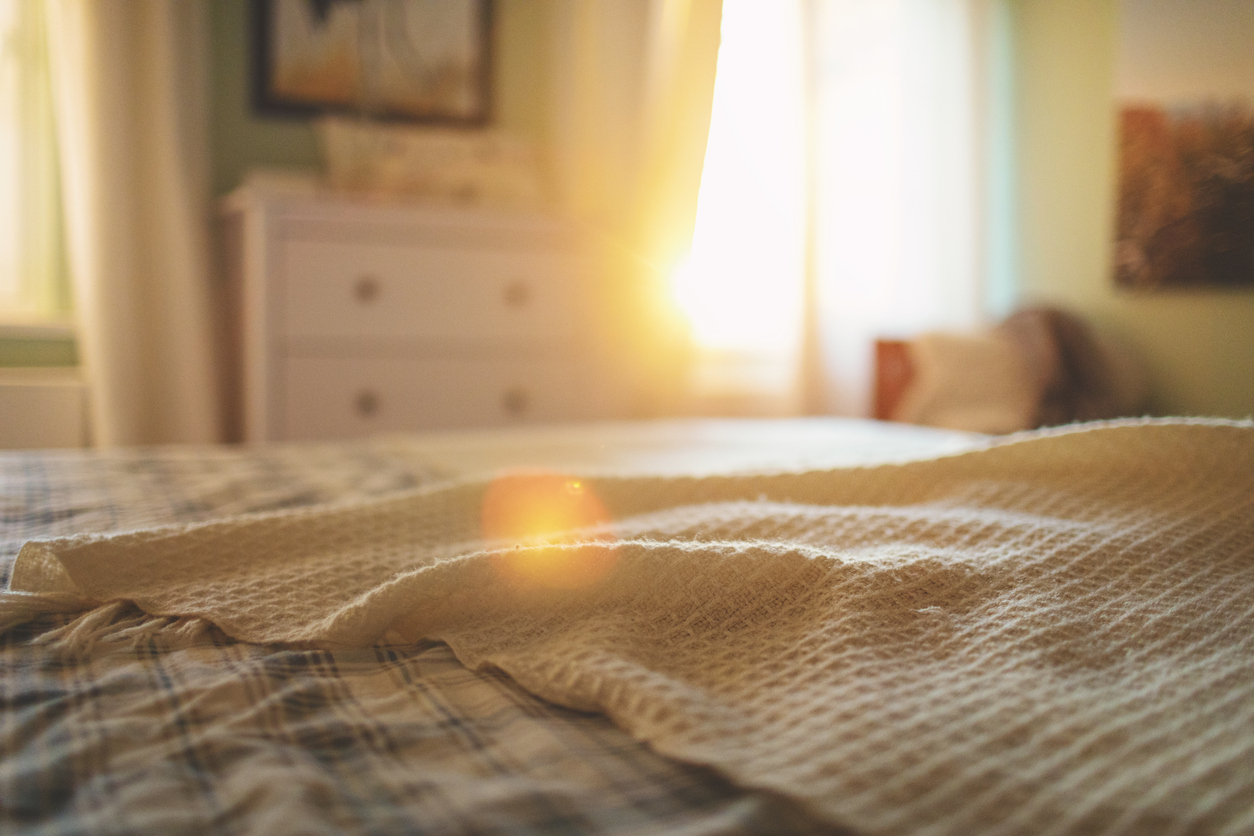 chambre à coucher avec lit au premier plan et lumière du soleil à travers la fenêtre