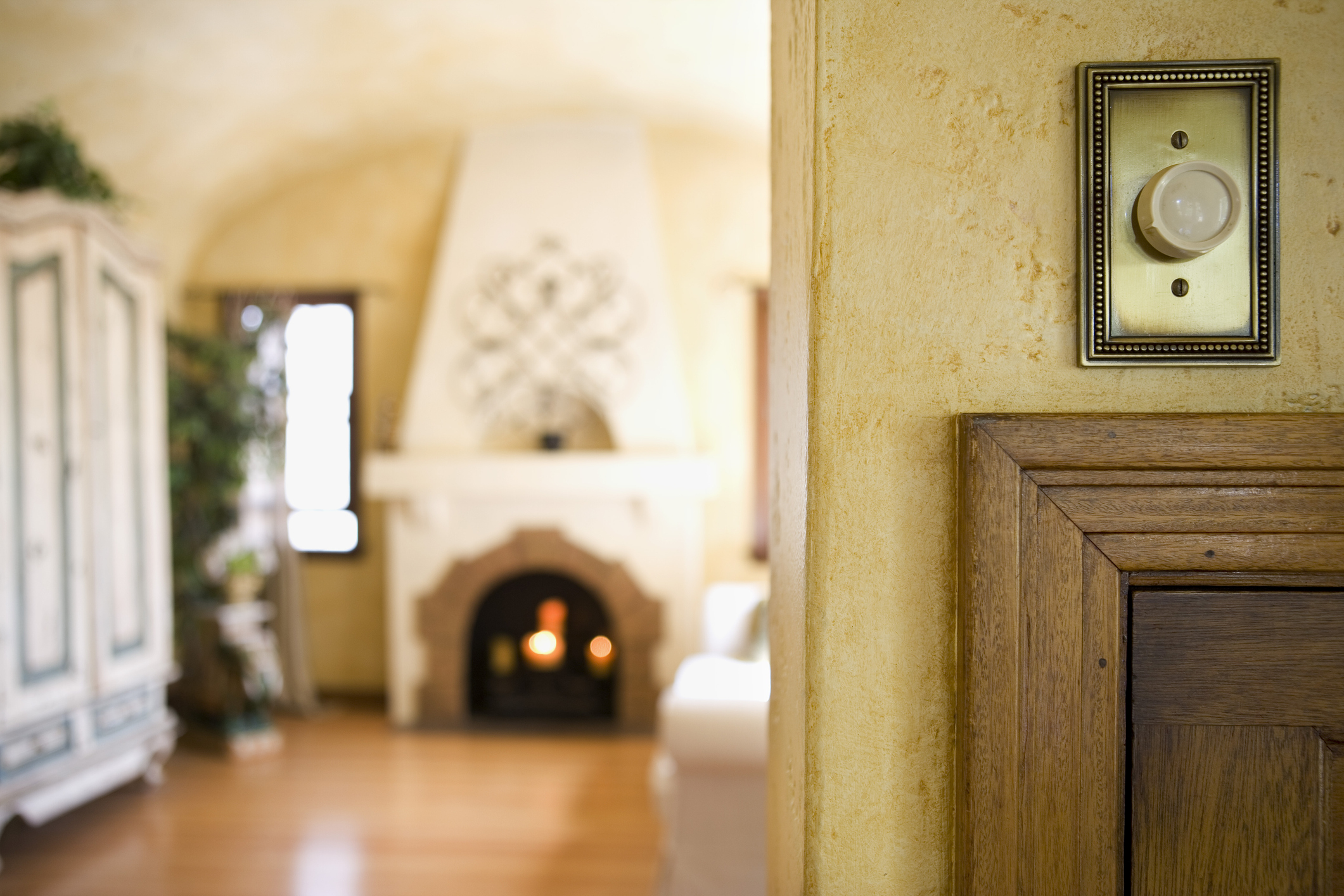 A brass switch plate is highlighted on a wall behind a living room with fireplace