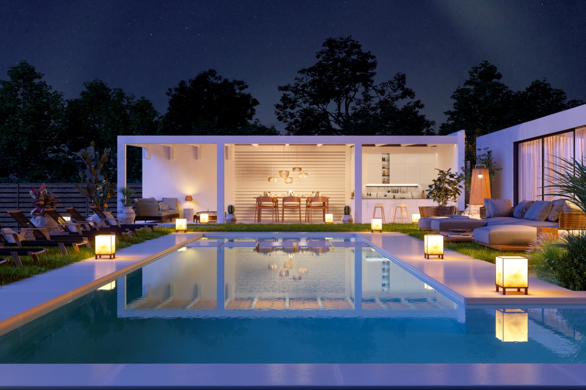 A modern home with a swimming pool lit by lantern lights on the pool deck. 