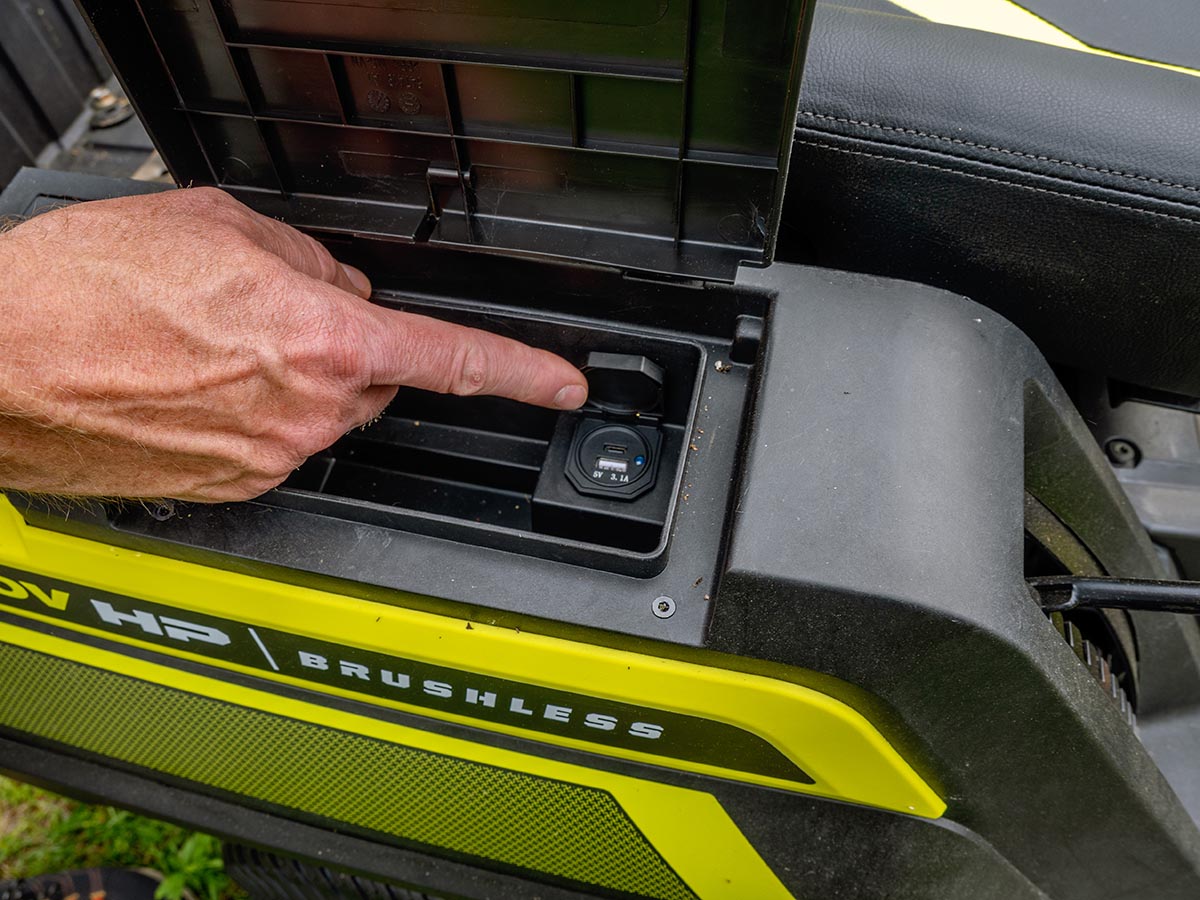 Hand pointing to device charging ports on Ryobi Electric Lawn Tractor