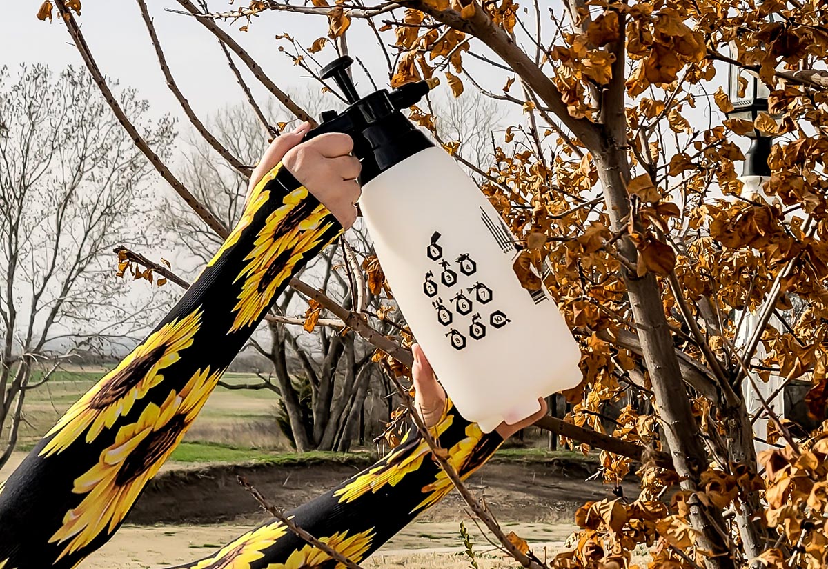 Photo of a woman's forearms clad in Wellday gardening sleeves for protection while spray a tree