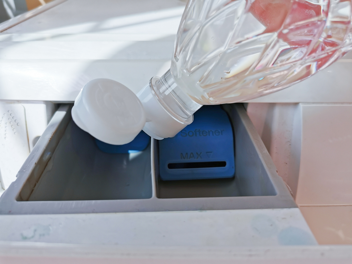 Une personne verse du vinaigre dans le bac d'un lave-linge.