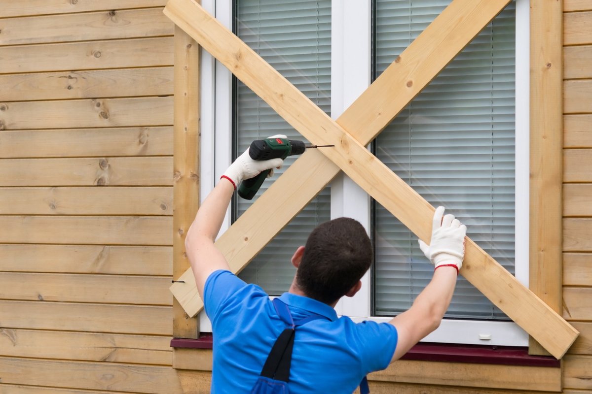 A person boards up a window of a home. 