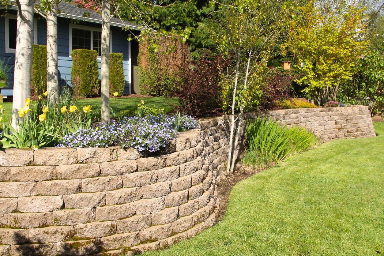 A beautiful retaining wall surrounded by plants and flowers in bloom.