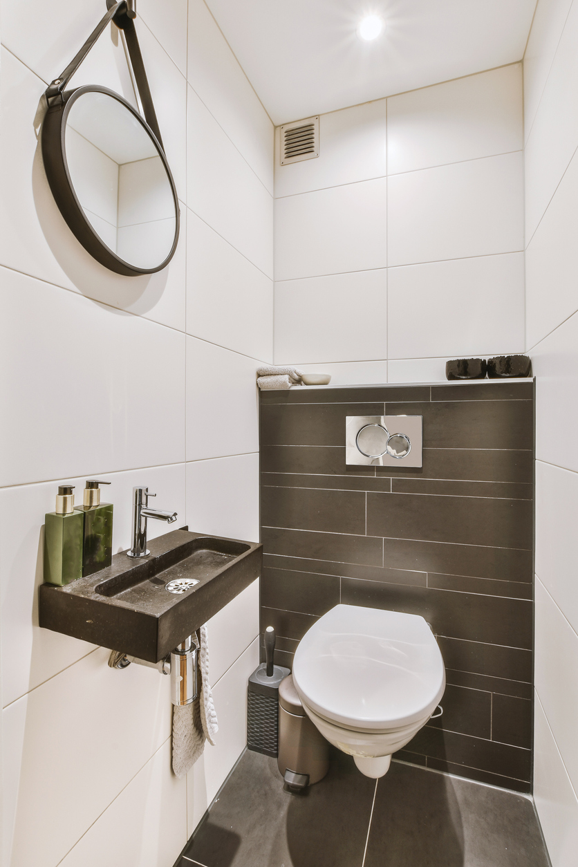 A very narrow half-bathroom with white walls and a dark-gray tile accent wall.