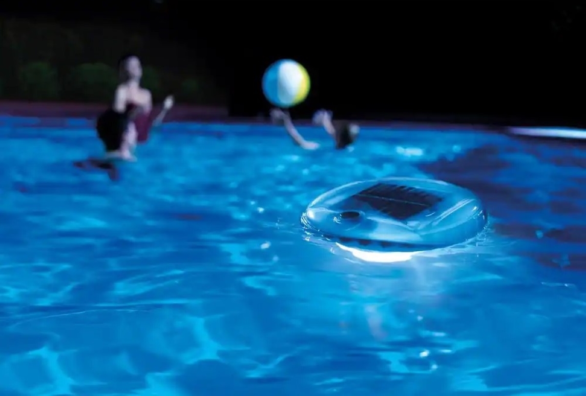 People play in pool at nighttime with a floating pool light.