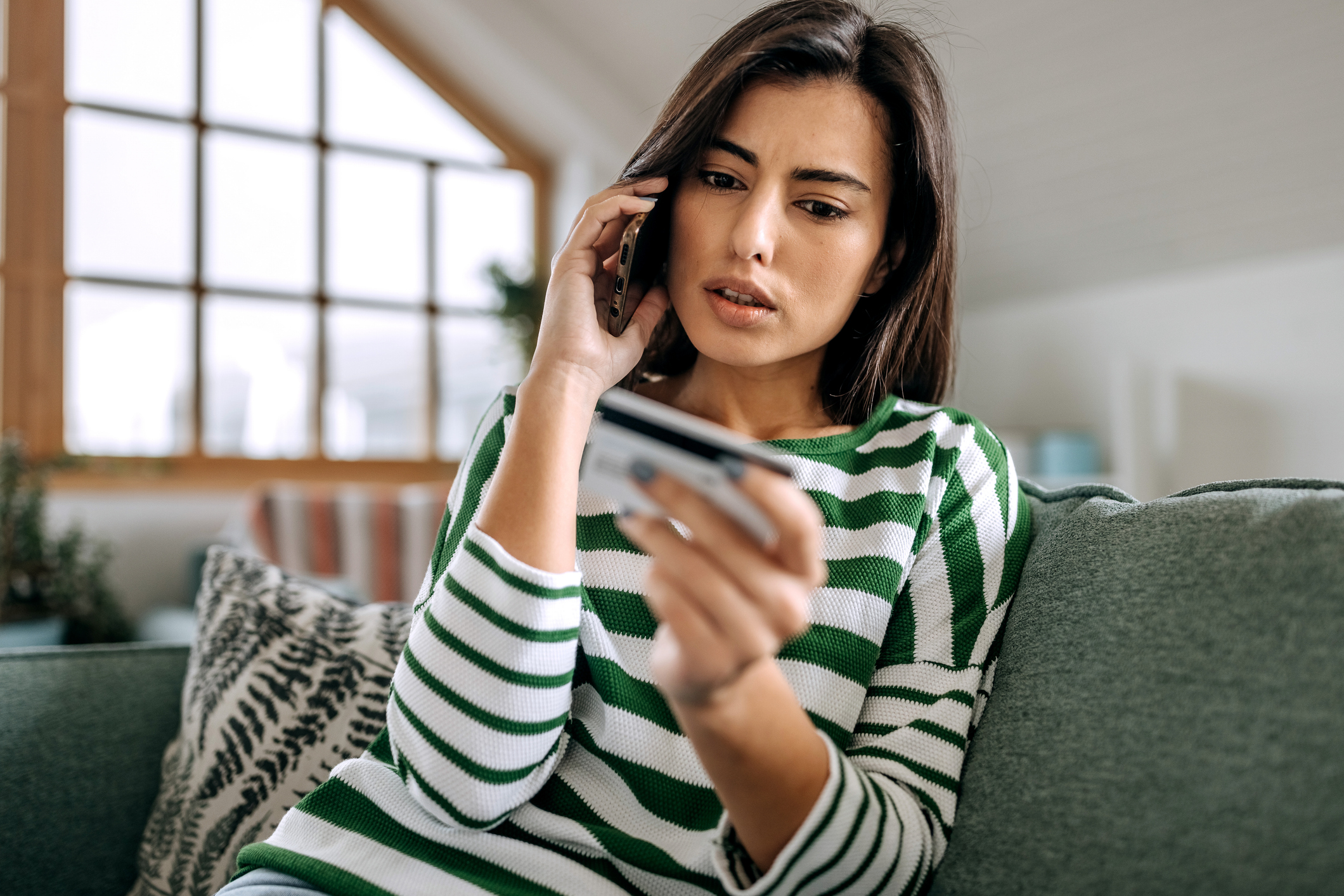 Une femme visiblement bouleversée ou confuse parle au téléphone tout en regardant sa carte de crédit.