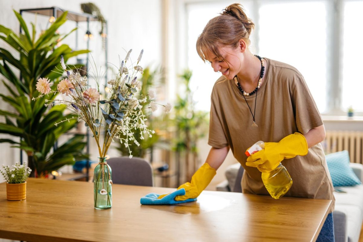 A view of a woman in yellow cleaning gloves wiping down a table. 