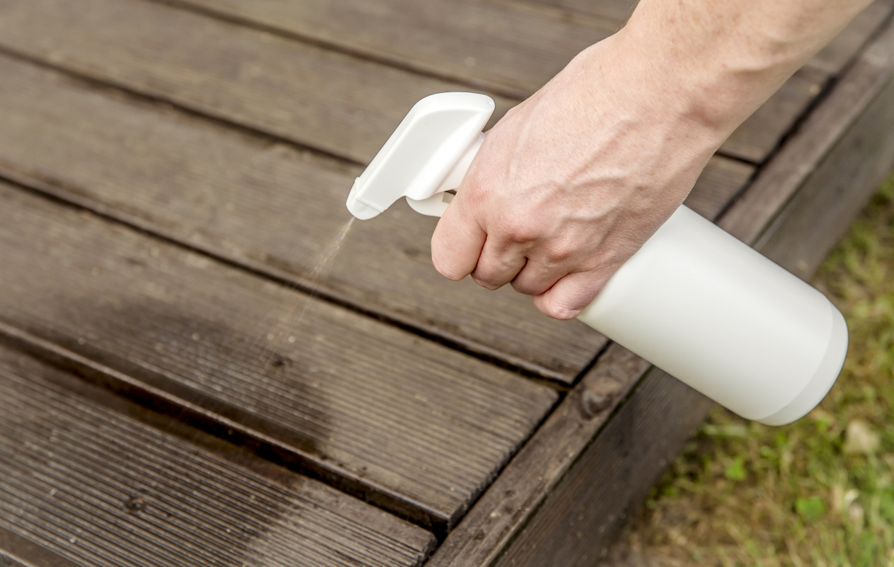 Homemade ant repellent spray mixture in bottle. Person hand spraying insect repellent on home terrace wood boards.