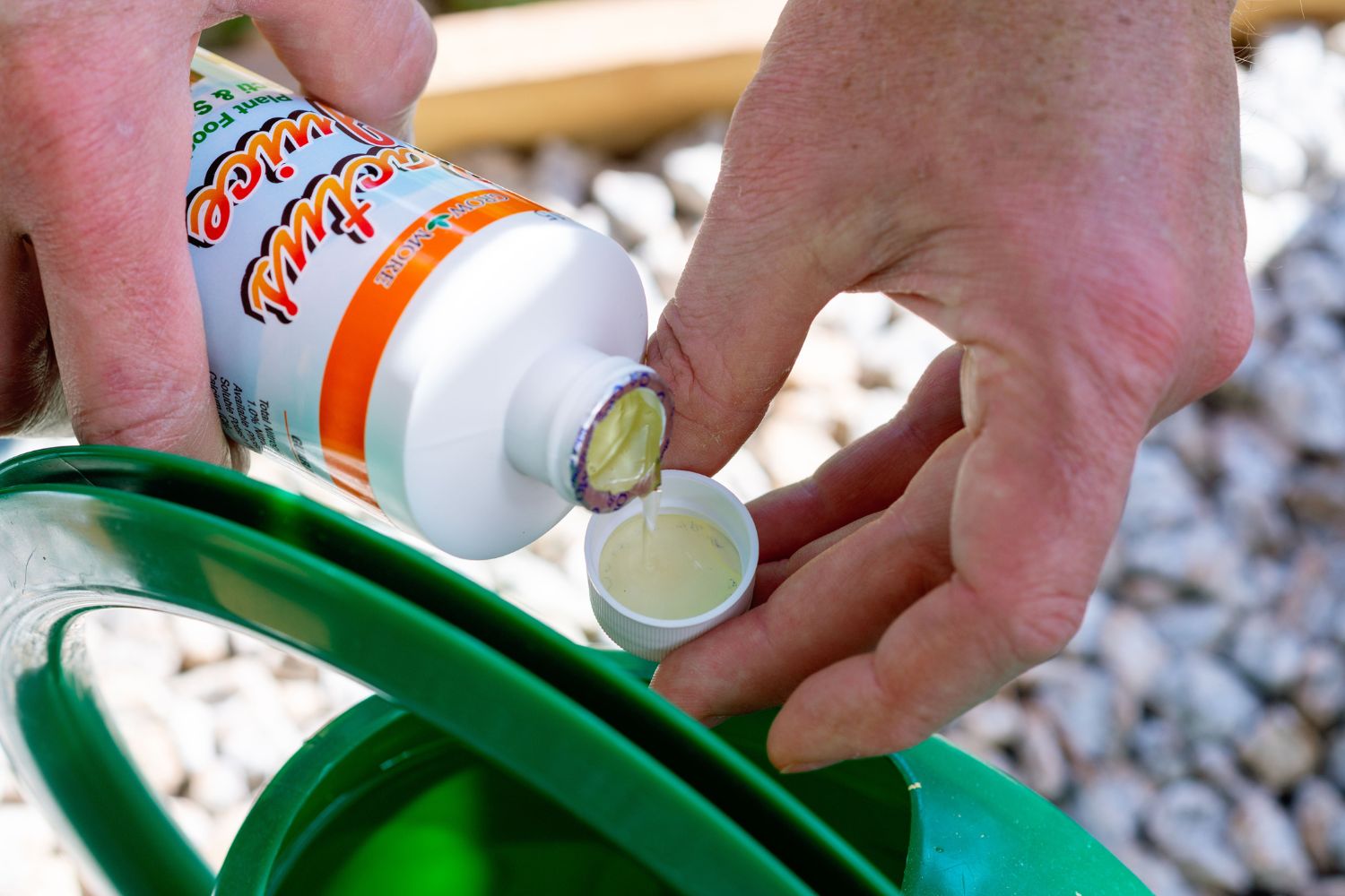 A bottle of plant fertilizer being poured into its cap above a water can