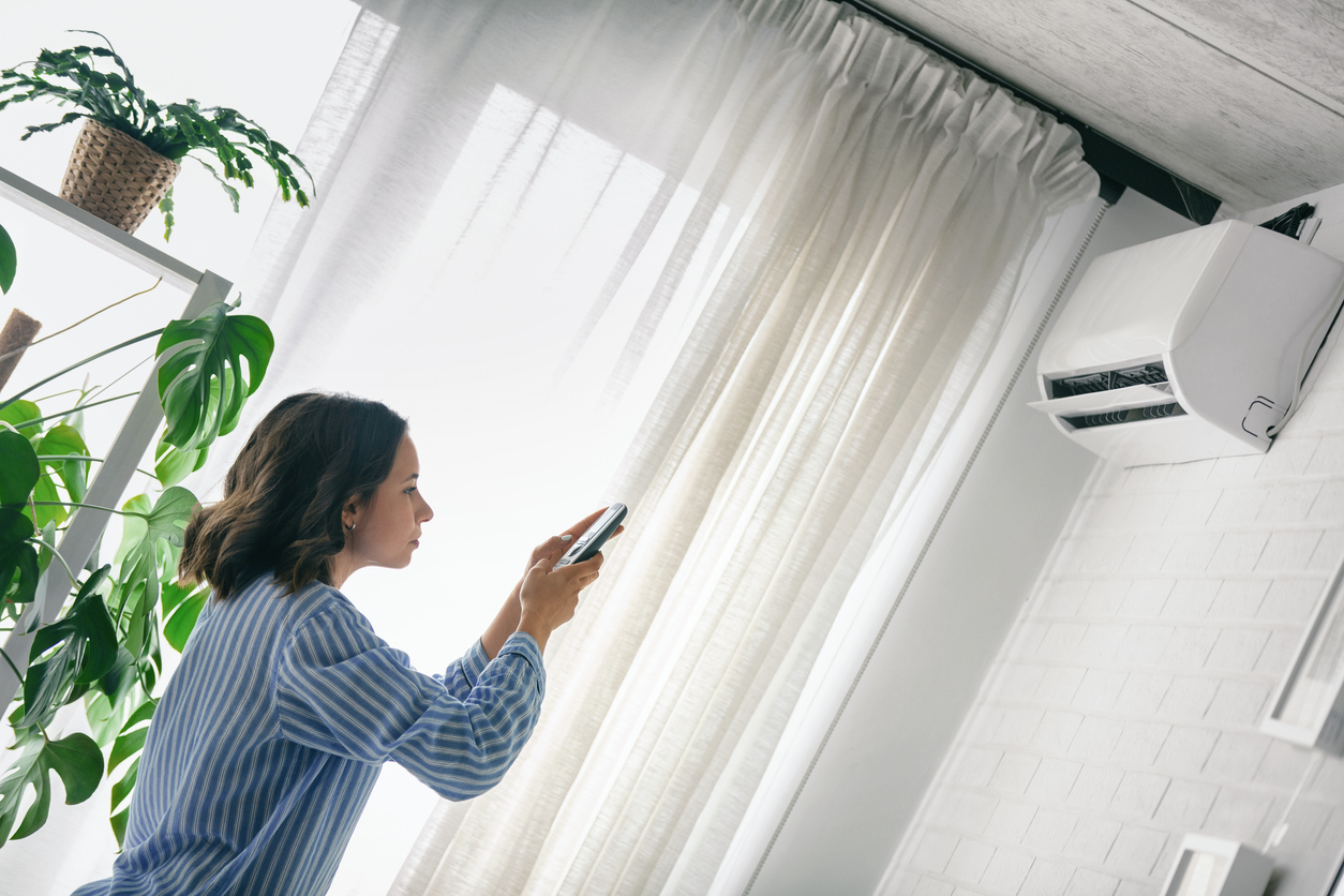 jeune femme utilisant une télécommande pour faire fonctionner le climatiseur monté en hauteur sur le mur dans un salon lumineux et aéré