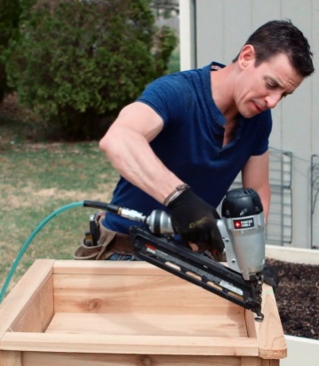 Un homme utilise une cloueuse de finition sur un projet de bois à l'extérieur.