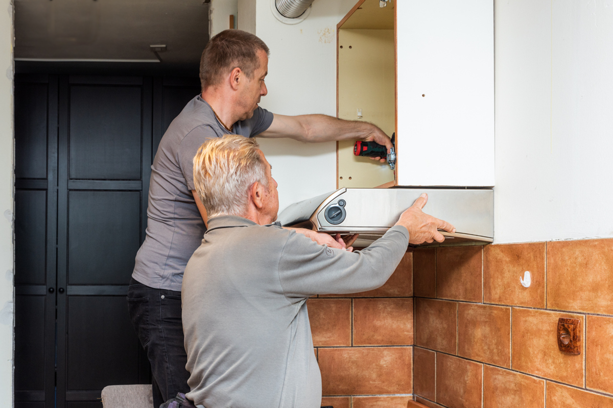 un homme aide un homme plus âgé à retirer la hotte de cuisine et l'armoire pour une élimination responsable lors d'une rénovation durable de la cuisine