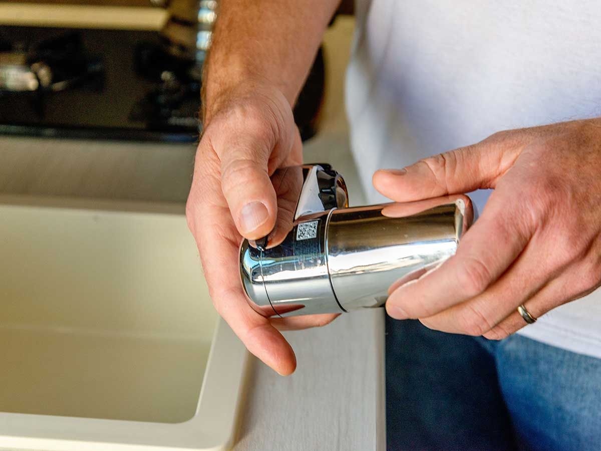 Une personne tenant dans ses mains le petit filtre pour robinet d'eau Brita Complete avant de l'installer.